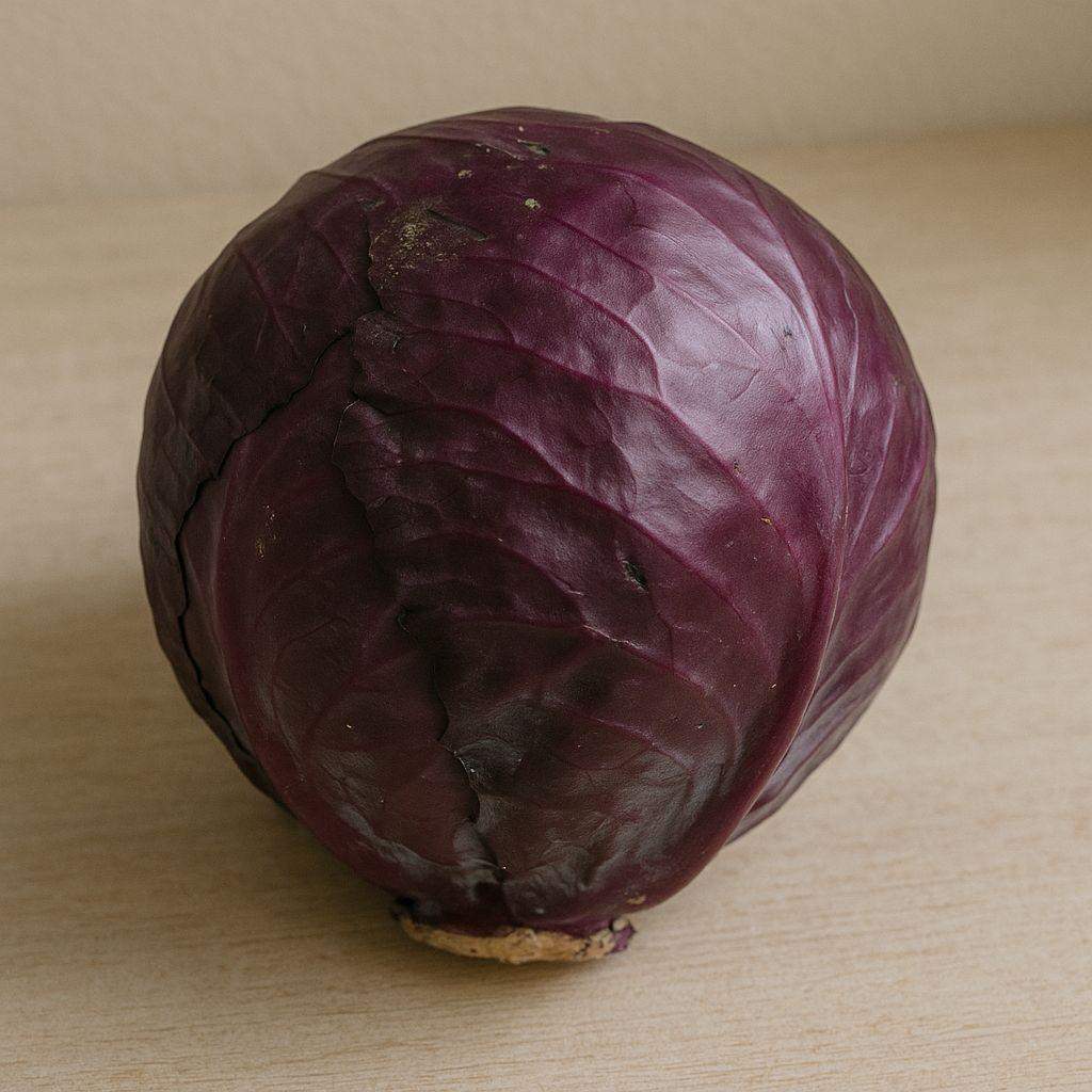 Czerwona kapusta na jasnym blacie, z widocznymi naturalnymi zagięciami i drobnymi skazami na liściach, w naturalnym świetle dziennym